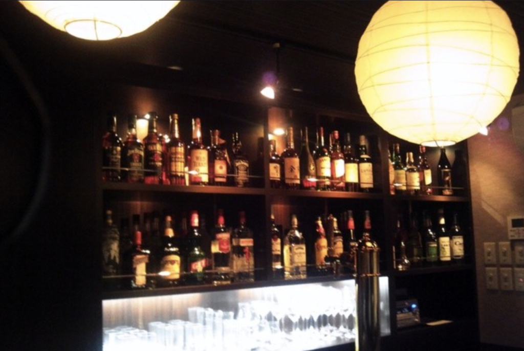 棚の中にグラスやお酒のボトルがたくさん並んでいて、天井には和風の丸い照明